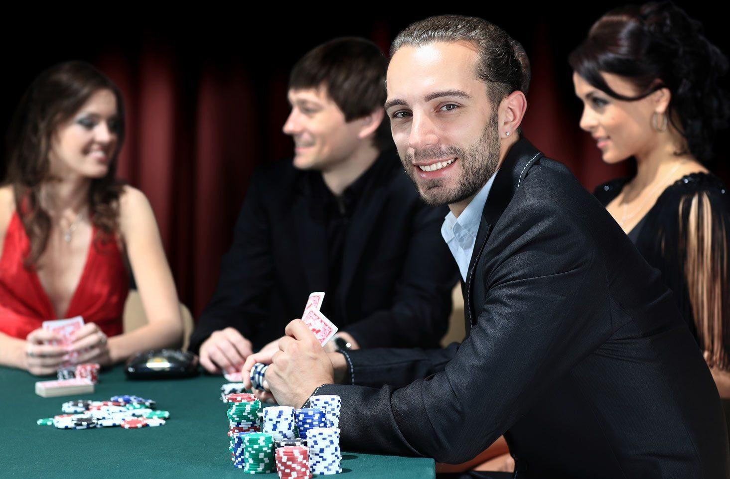 Well-dressed players at a green-felt poker table with tall chip stacks