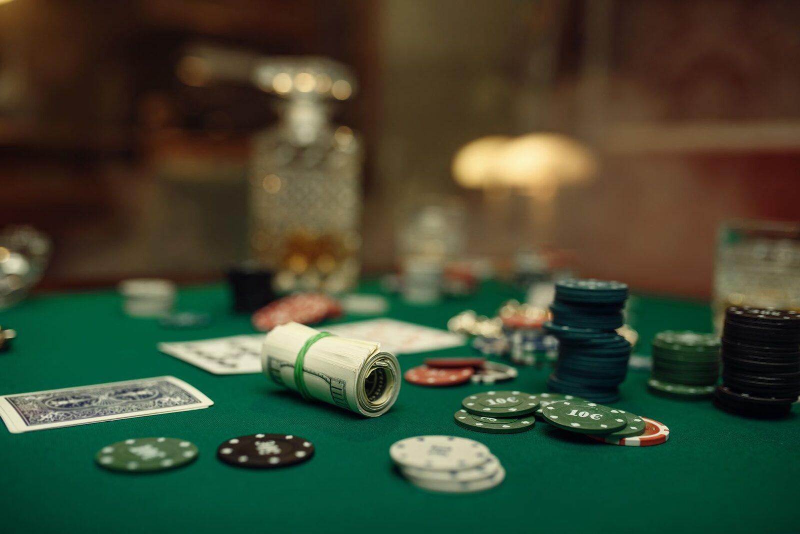 A roll of cash beside poker chips on a green felt home poker table