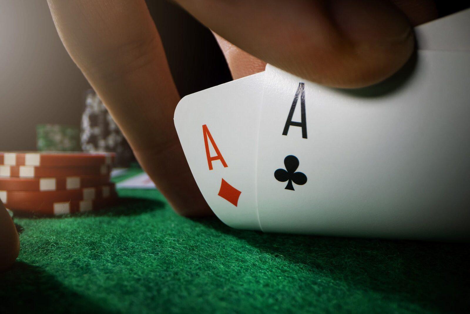 A player lifting the corner of two ace hole cards beside red poker chips